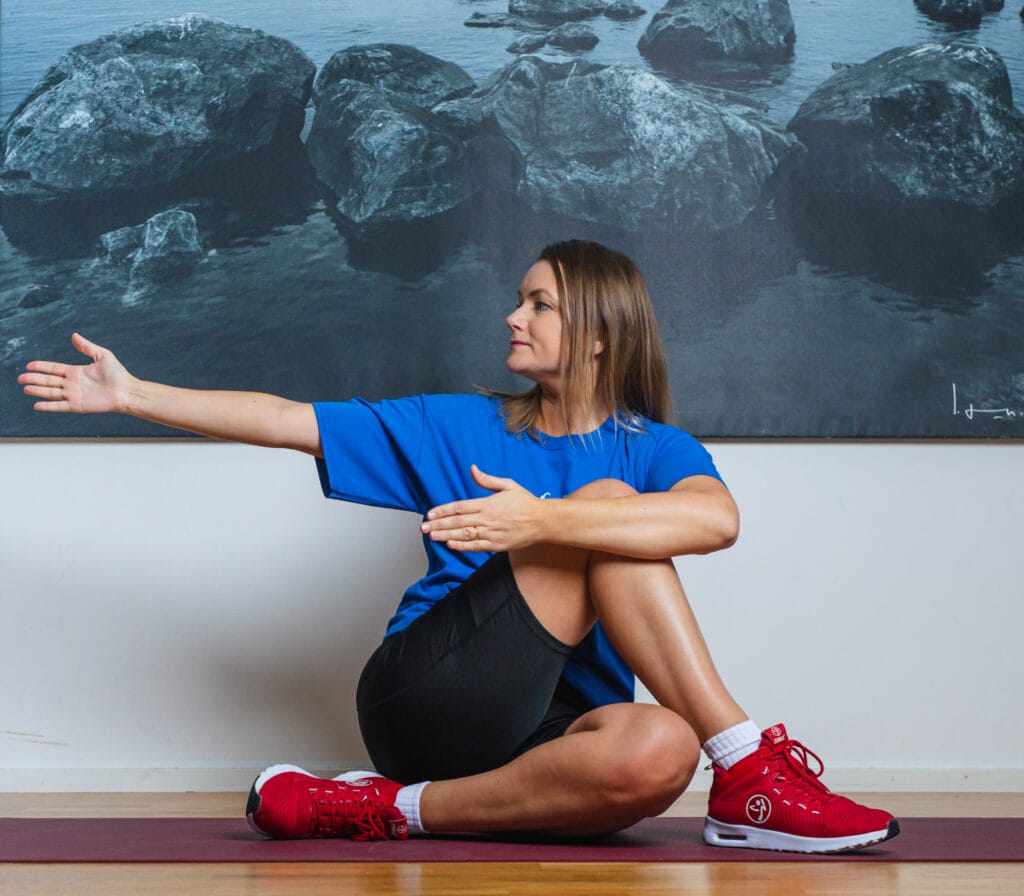 Kvinna i blå t-shirt och svarta shorts stretchar på yogamatta.