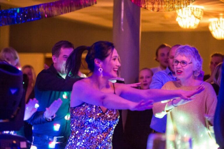 Kvinnor dansar och skrattar på en fest med färgglada lampor.