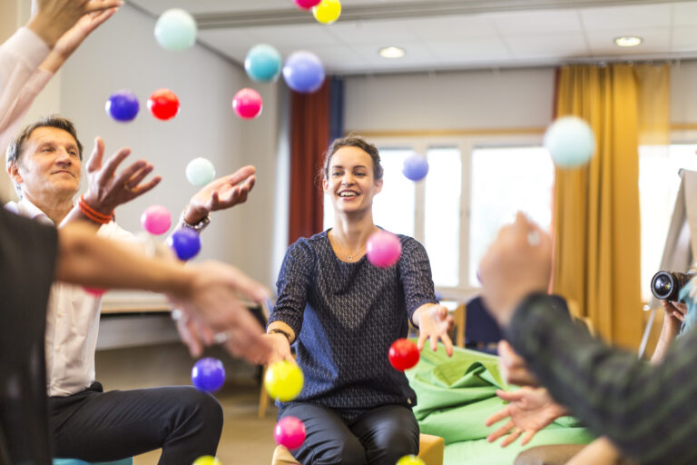 Människor kastar färgglada bollar i luften som en del av en gruppaktivitet.